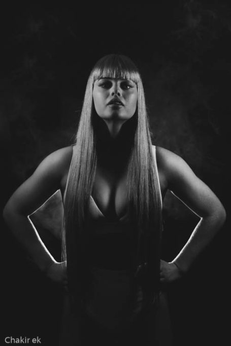 Portrait of a woman with long hair, standing confidently against a dark background.